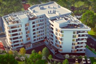 SBM 2024 Reference Values Vista aérea de um moderno edifício de apartamentos de médio porte com um formato único e irregular promovendo moradia saudável. Ele possui várias varandas e um terraço na cobertura. A área ao redor é exuberante com árvores, gramados e alguns prédios menores, promovendo viver saudável.