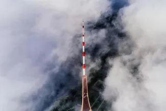 Uma alta torre de comunicação vermelha e branca atravessa as nuvens ao redor, com uma vista aérea do terreno florestal e uma paisagem que promove viver saudável parcialmente visível abaixo.