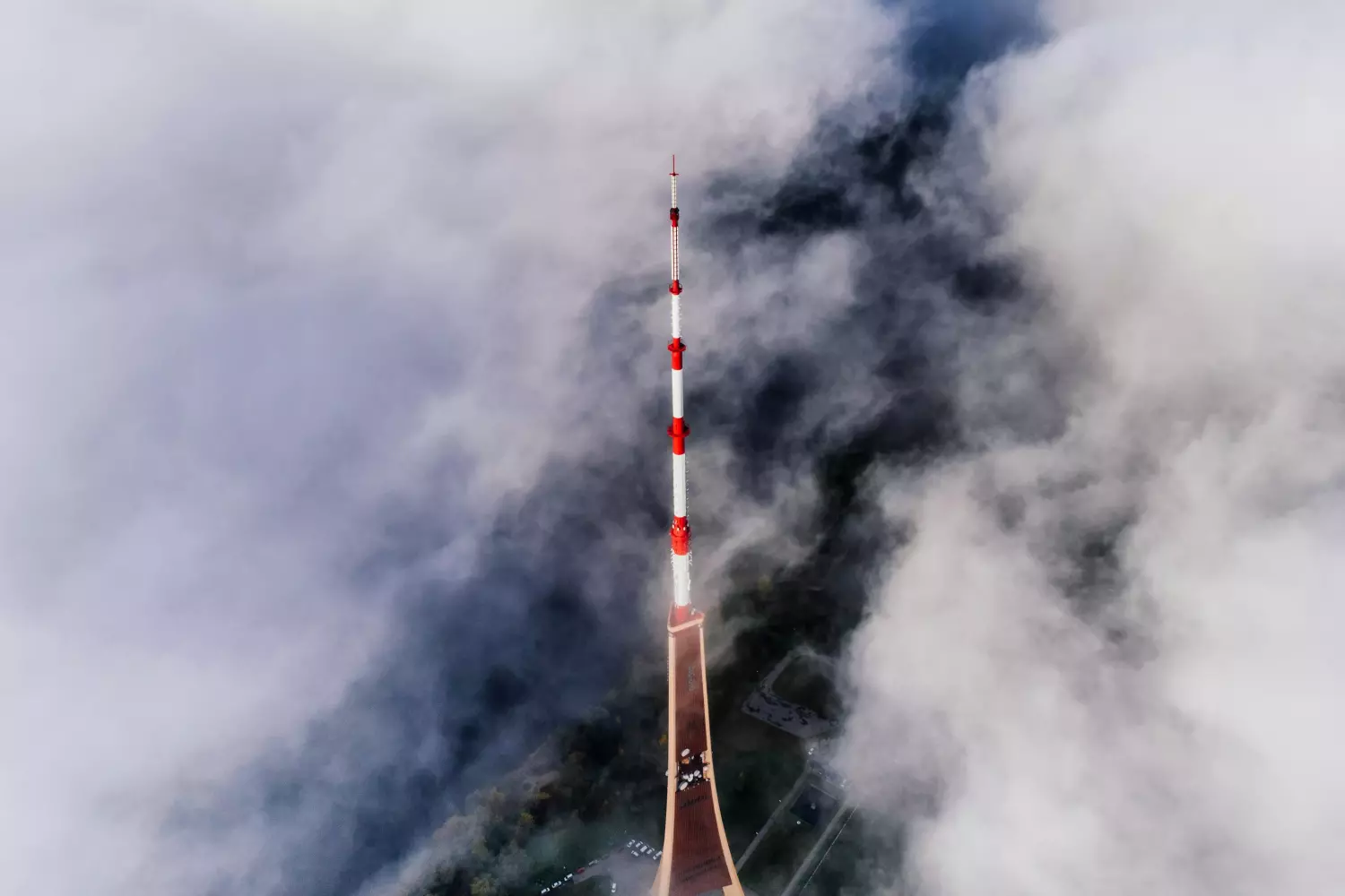 Uma alta torre de comunicação vermelha e branca atravessa as nuvens ao redor, com uma vista aérea do terreno florestal e uma paisagem que promove viver saudável parcialmente visível abaixo.
