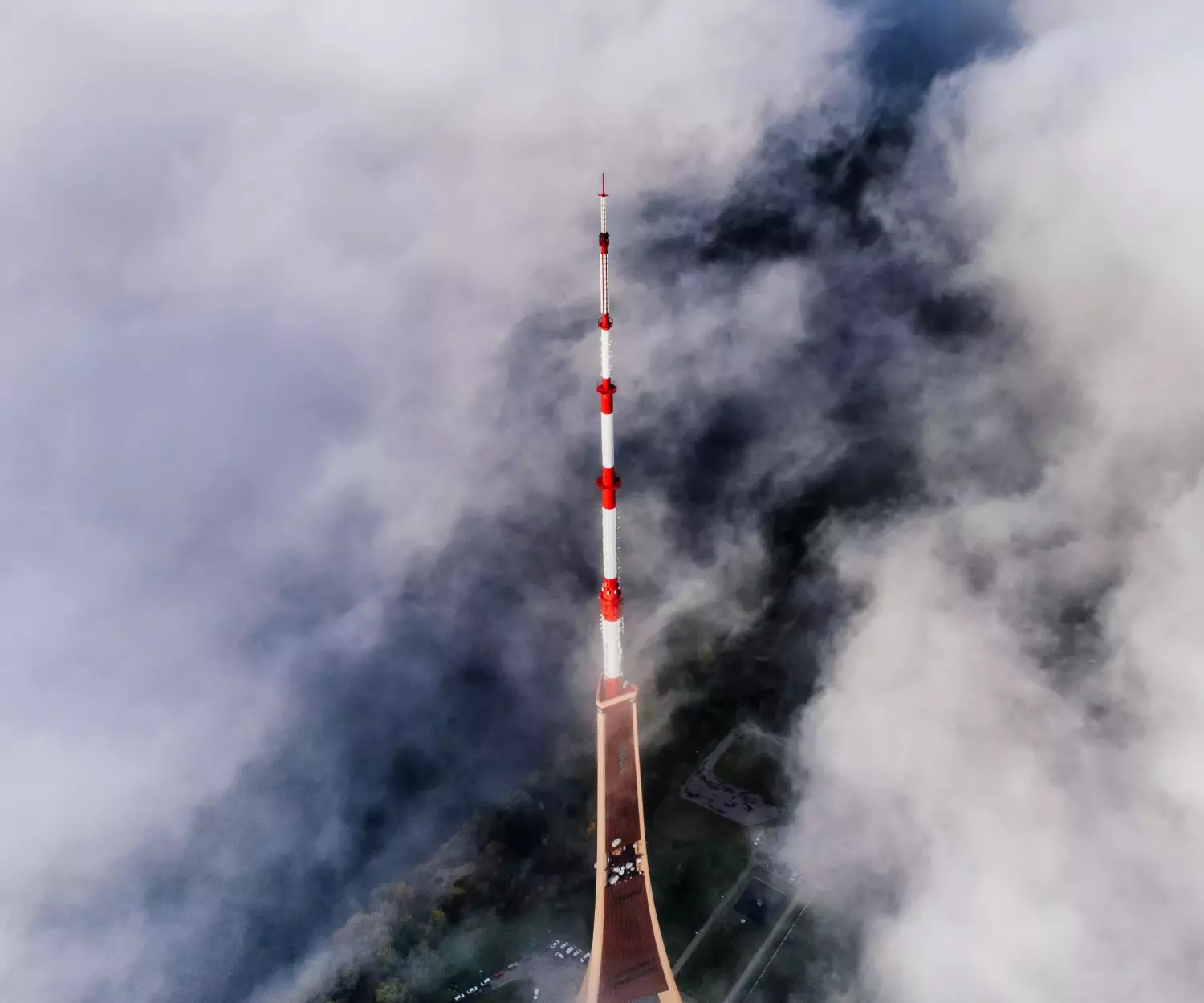 Uma alta torre de comunicação vermelha e branca atravessa as nuvens ao redor, com uma vista aérea do terreno florestal e uma paisagem que promove viver saudável parcialmente visível abaixo.