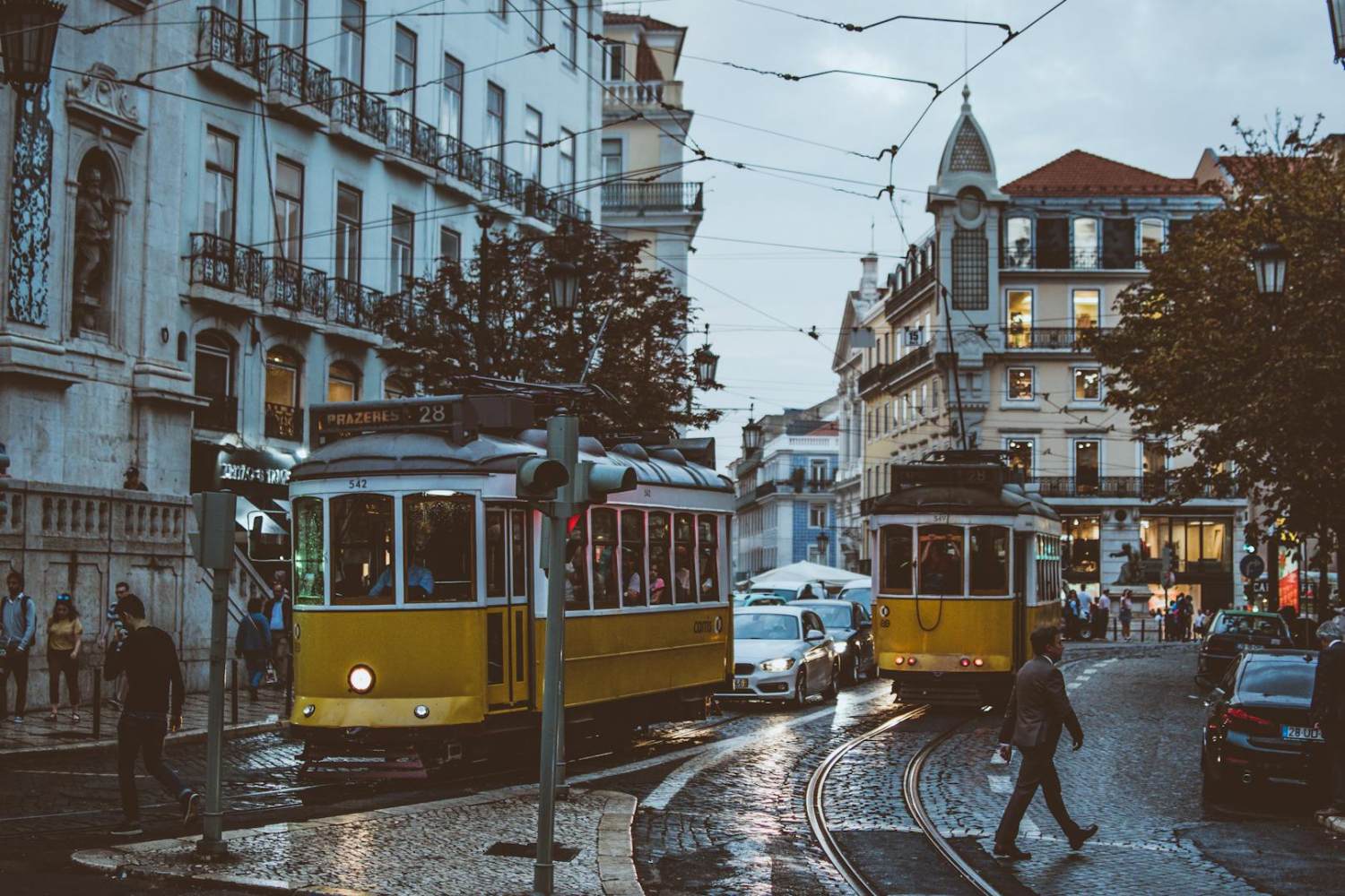 WELL & LEED Scenic view of trams navigating the charming streets of Lisbon at dusk, capturing urban life and transportation.