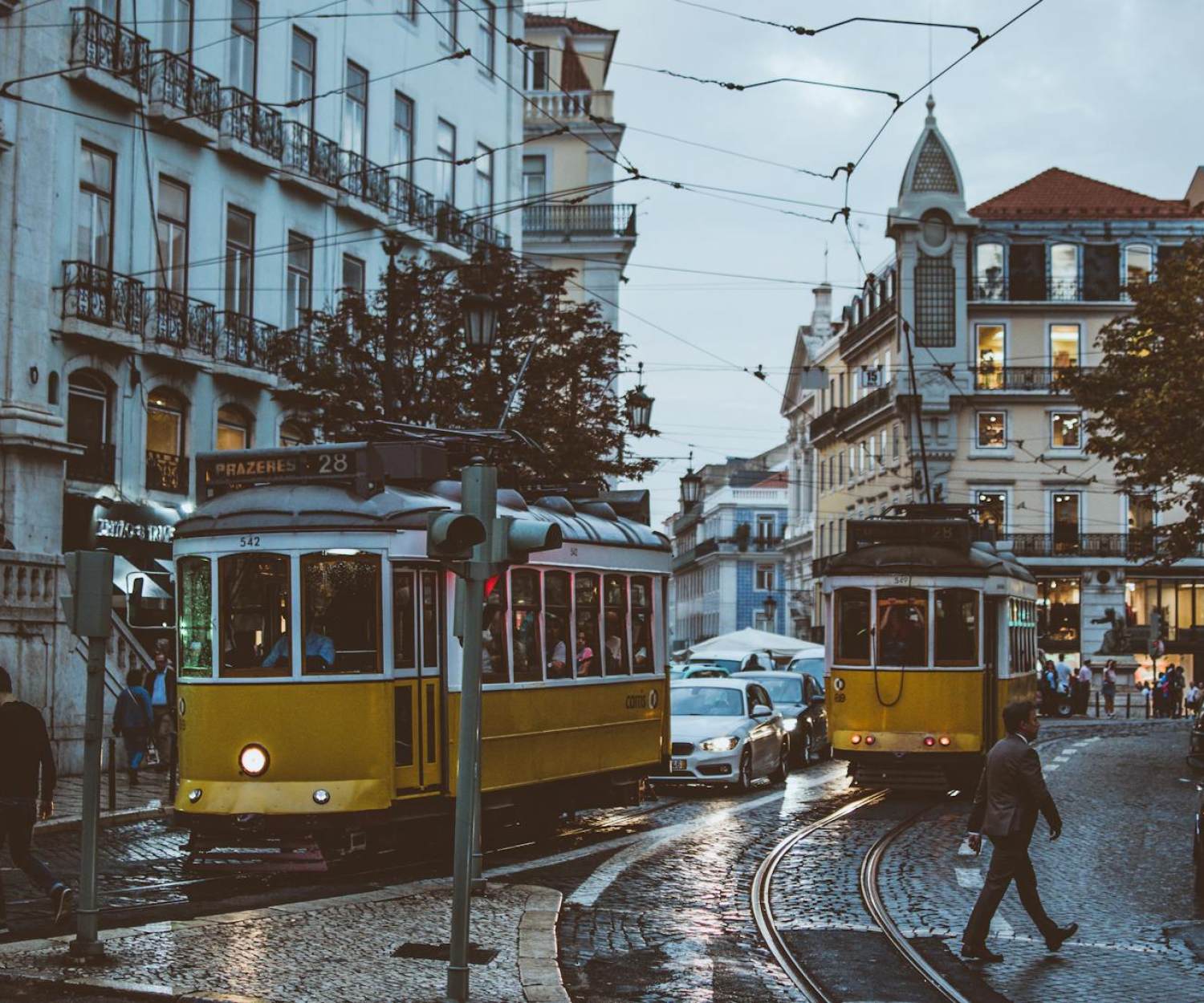 WELL & LEED Scenic view of trams navigating the charming streets of Lisbon at dusk, capturing urban life and transportation.